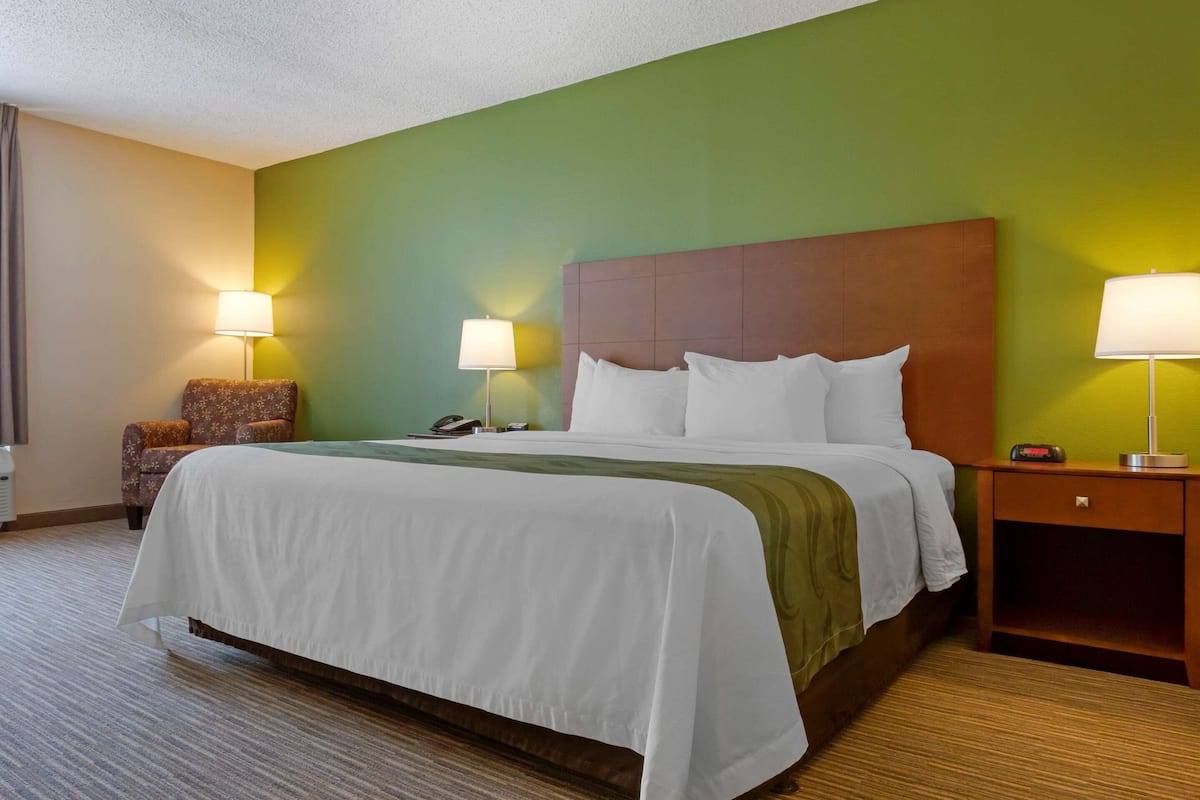 A hotel room with a large bed, two bedside lamps, a nightstand with a phone, and a chair.