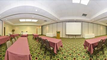 Un salón de conferencias con mesas, sillas, un atril y una pantalla de proyección.