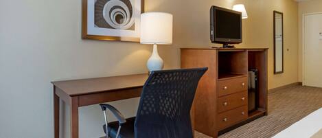 Een hotelkamer met een houten bureau, een zwarte bureaustoel, een witte lamp, een televisie op een houten kast en een kunstwerk in een lijst aan de muur.
