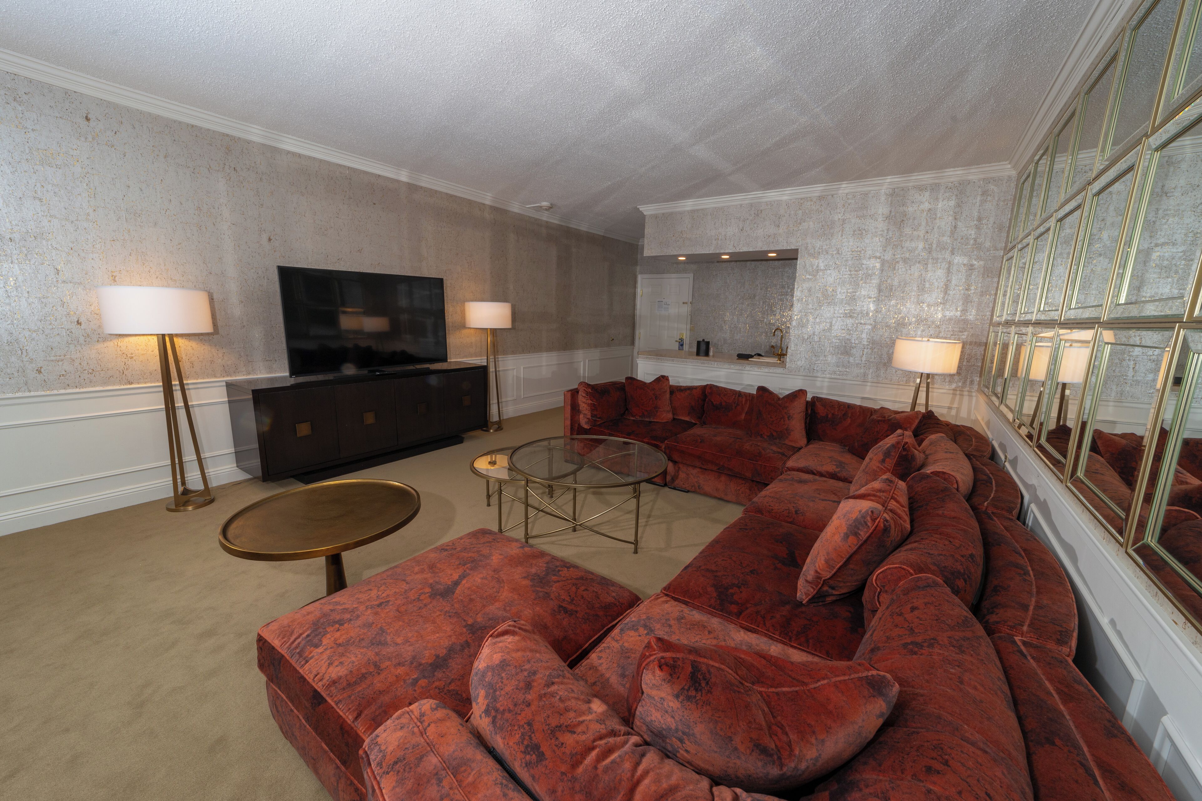 A spacious living room with a large red sectional sofa, a glass coffee table, and a flat-screen TV on a dark wooden cabinet.
