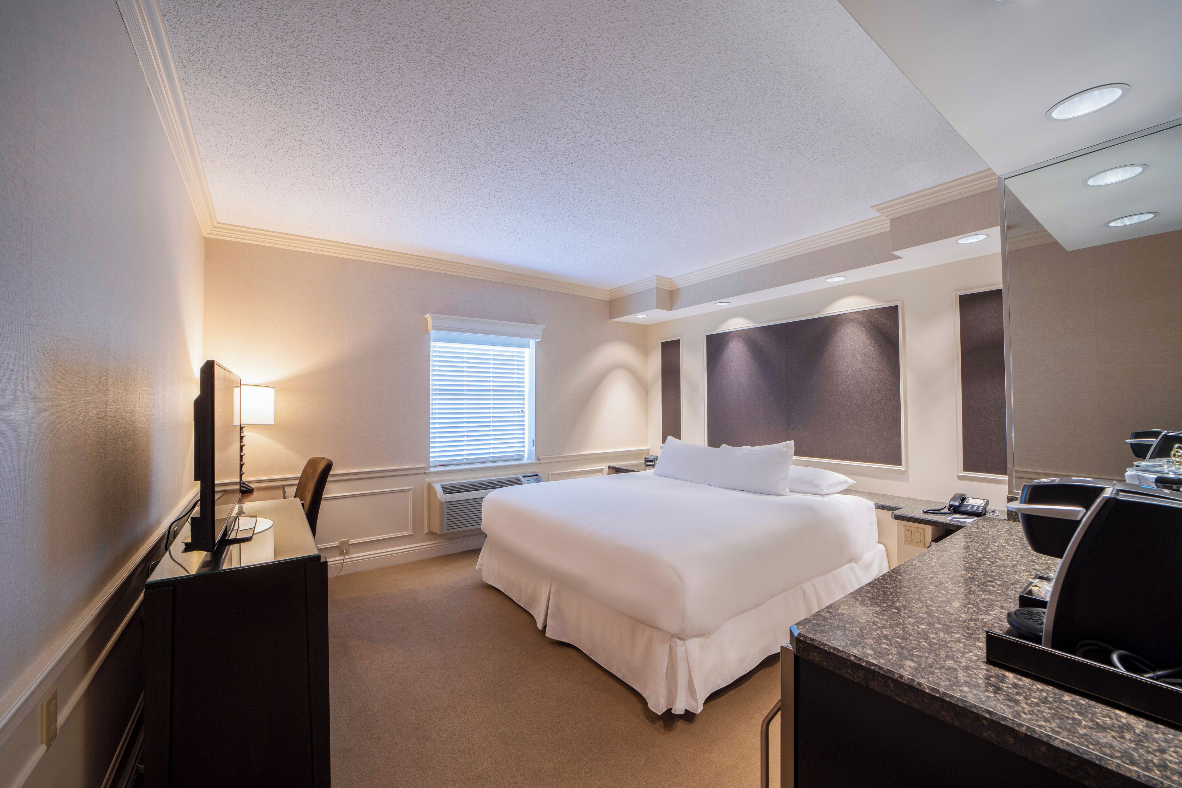Ein Hotelzimmer mit Bett, Schreibtisch, Stuhl und einem großen Spiegel.