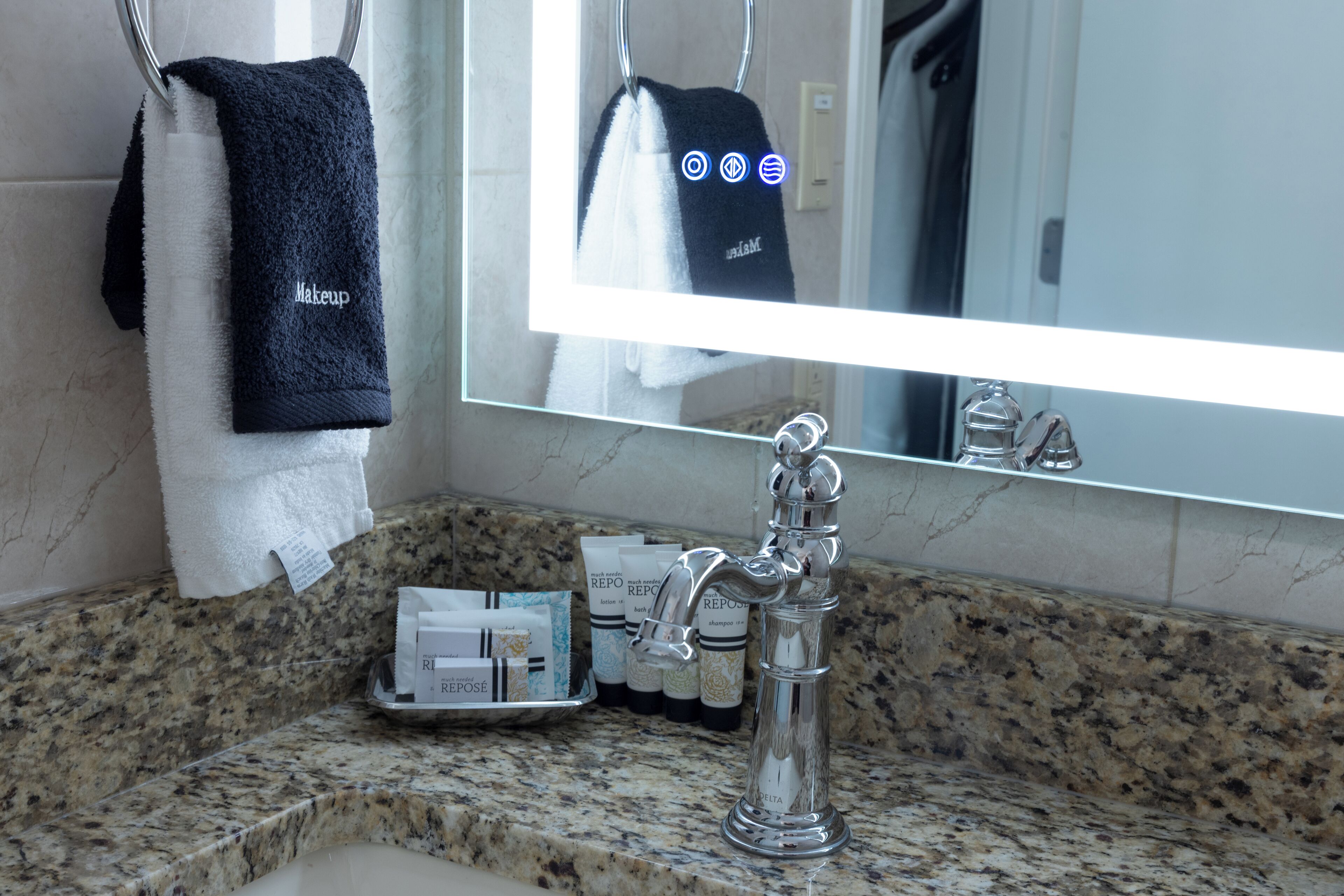 A bathroom with a granite countertop, a chrome faucet, and a mirror reflecting a towel and toiletries.