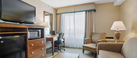 Una camera d'albergo con schermo piatto, forno a microonde, frigorifero, scrivania con sedia, divano e lampada.
