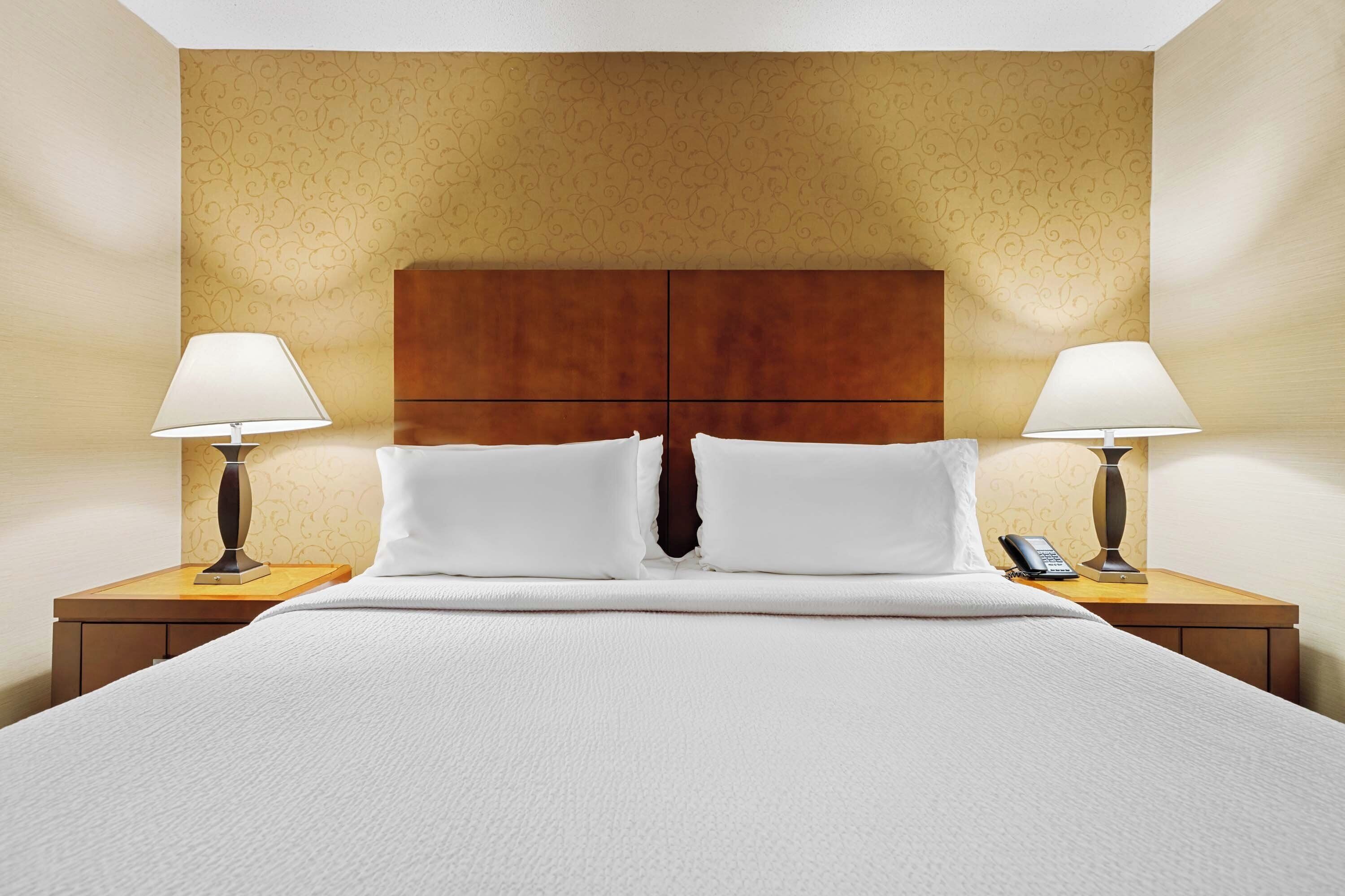 Hotelkamer met een groot bed, twee nachtkastjes met lampen, een houten hoofdeinde en een behang met een patroon.