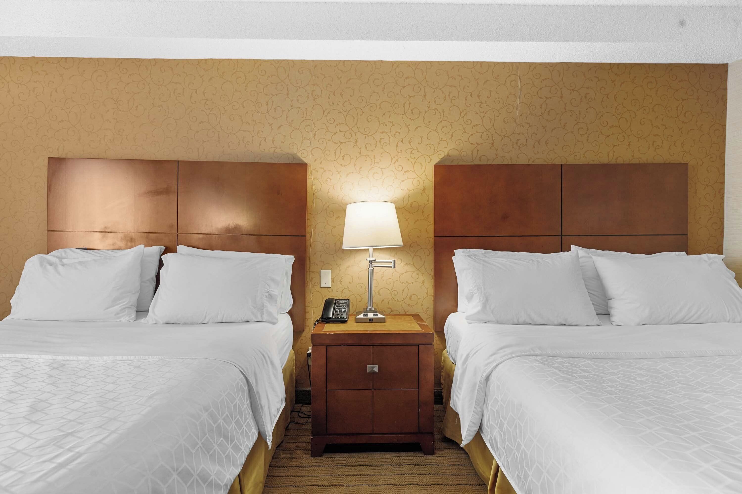 Une chambre d’hôtel avec deux lits, une table de chevet avec une lampe et un téléphone.