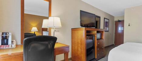 A hotel room with a desk, chair, television, dresser, and bed.