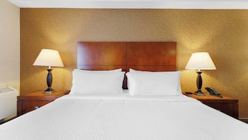 Quarto de hotel com uma cama grande, duas mesas de cabeceira com abajures, uma cabeceira de madeira e um papel de parede estampado.