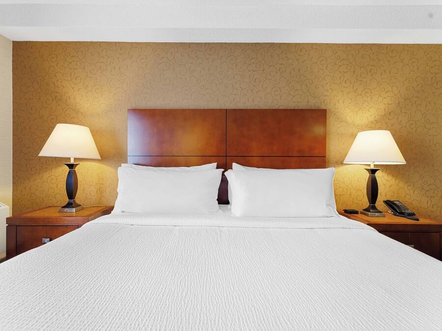 Camera d'albergo con un letto grande, due comodini con lampade, una testiera in legno e una parete decorata.