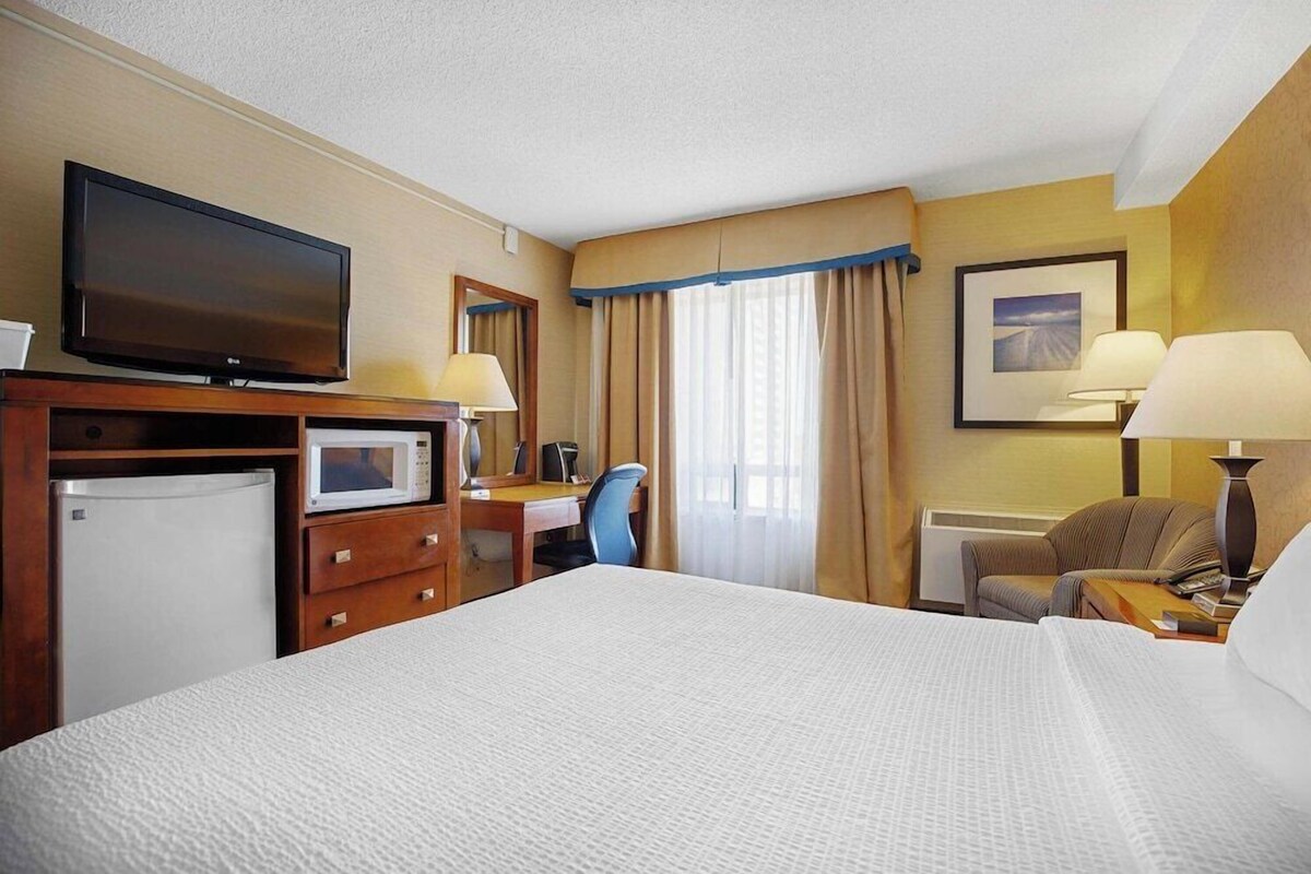 A hotel room with a large bed, a desk with a computer, a television, a microwave, and a refrigerator.