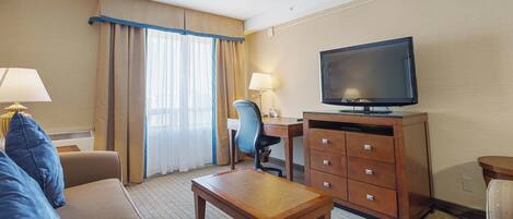 Habitación de hotel con sofá, una mesa de centro de madera, escritorio con silla, televisor y cómoda.