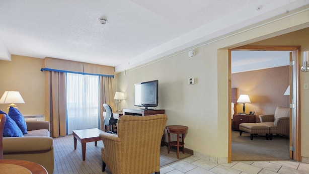 A hotel room with a sofa, armchair, TV, desk, and a small table.