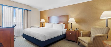 Una habitación de hotel con una cama grande, dos mesitas de noche con lámparas, un aparador de madera, una silla y un escritorio con teléfono.