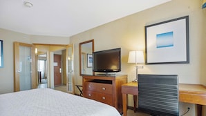 A hotel room with a large bed, a desk, a chair, a television, and a framed picture on the wall.