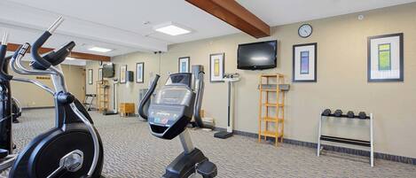 Un gimnasio con equipamiento de ejercicio, un televisor, fotografías enmarcadas y un reloj en la pared.
