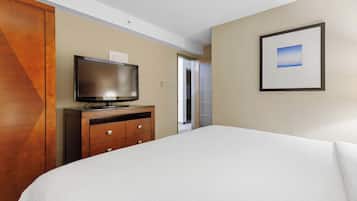 Habitació d'hotel amb un llit, una televisió sobre una petita estant de fusta, un quadre amb marc a la paret i una porta que condueix a una altra habitació.