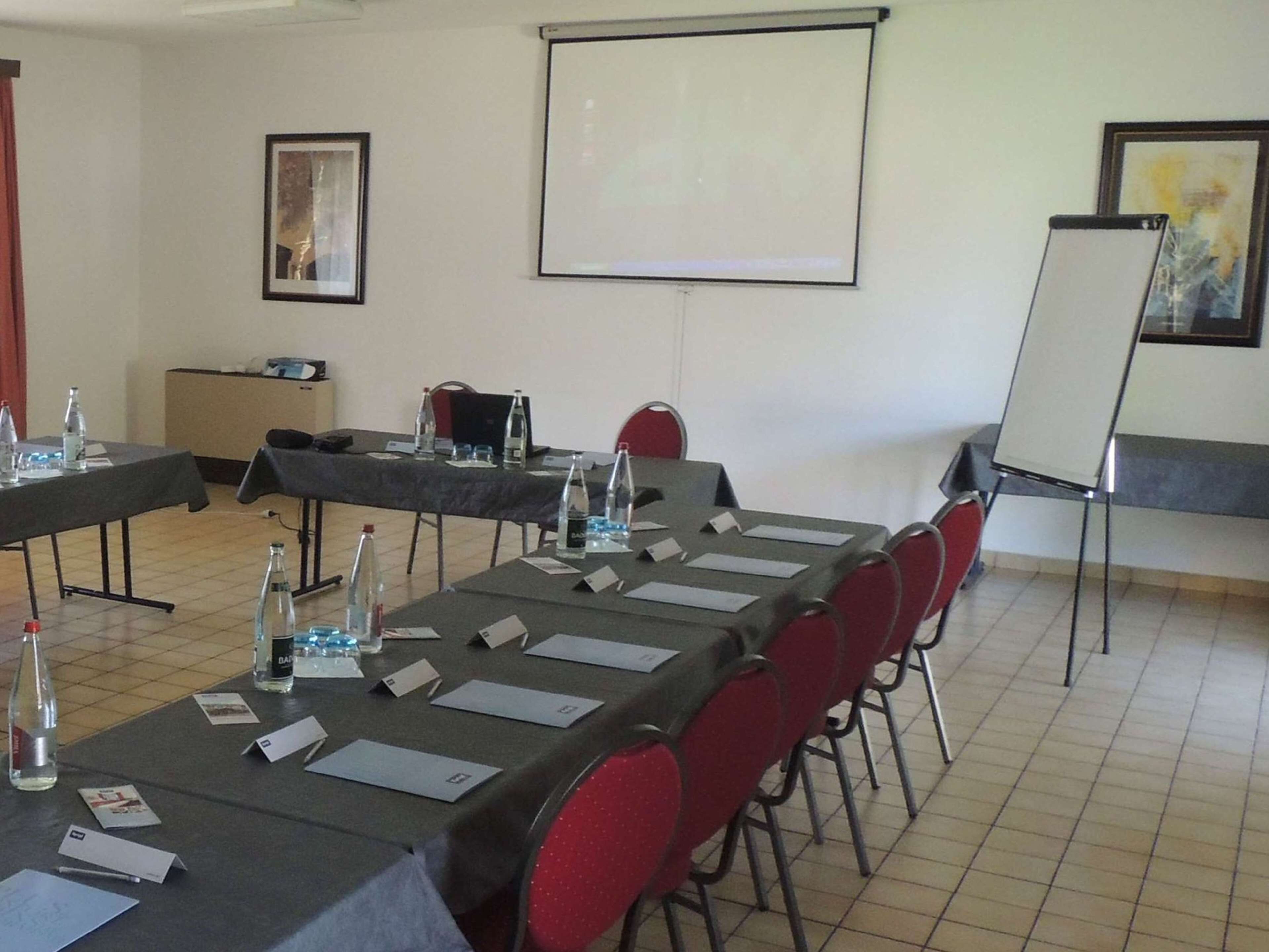 A conference room with long tables, chairs, name cards, water bottles, and a projector screen.