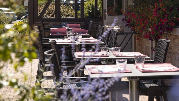 An outdoor dining area with tables and chairs, a covered seating area, and a building with a tiled roof.
