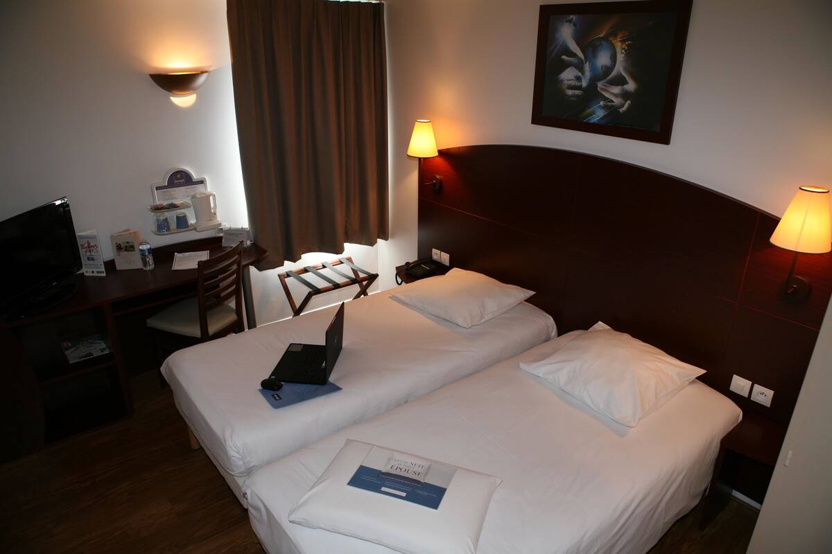 A hotel room with two beds, a desk with a laptop, a coffee maker, and a TV.