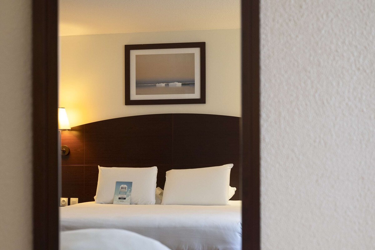 A hotel room with a bed, a nightstand, and a wall-mounted lamp.