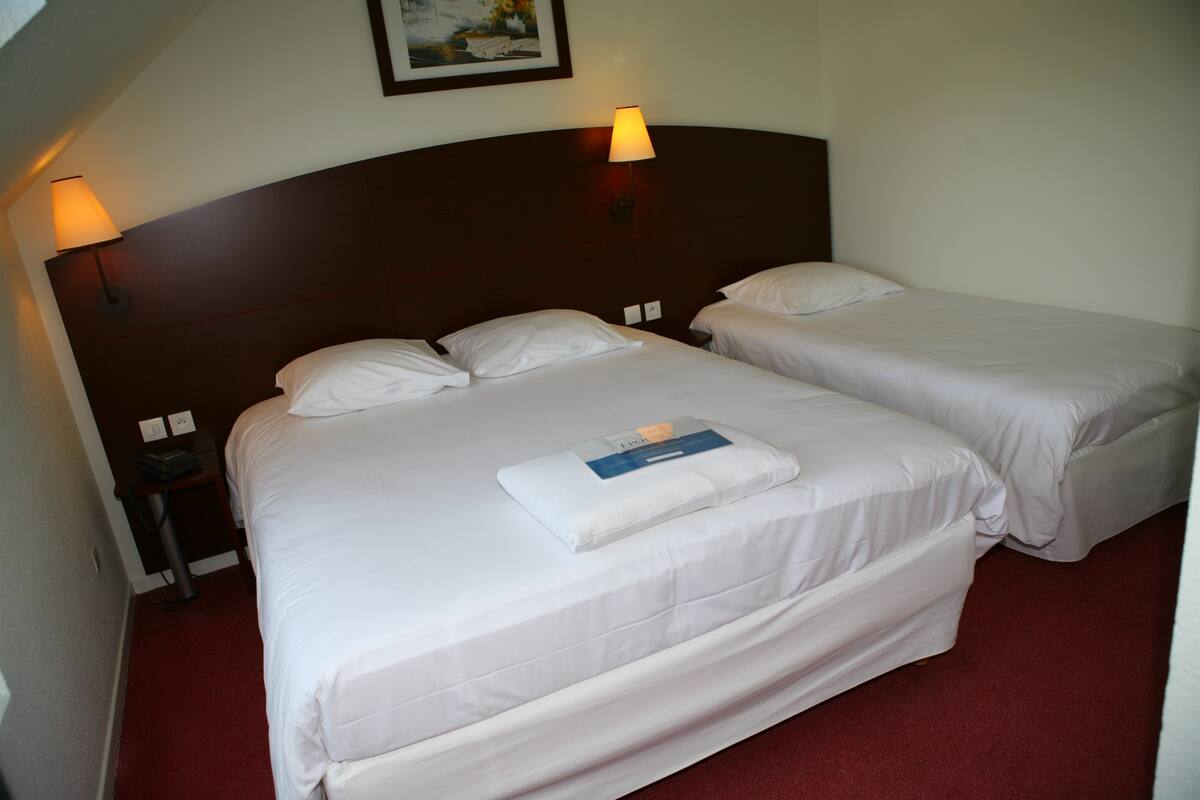 A hotel room with two beds, a wooden headboard, a red carpet, and a painting on the wall.