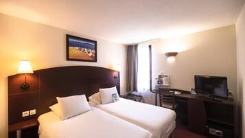A hotel room with two beds, a desk with a television, a lamp, and a painting on the wall.