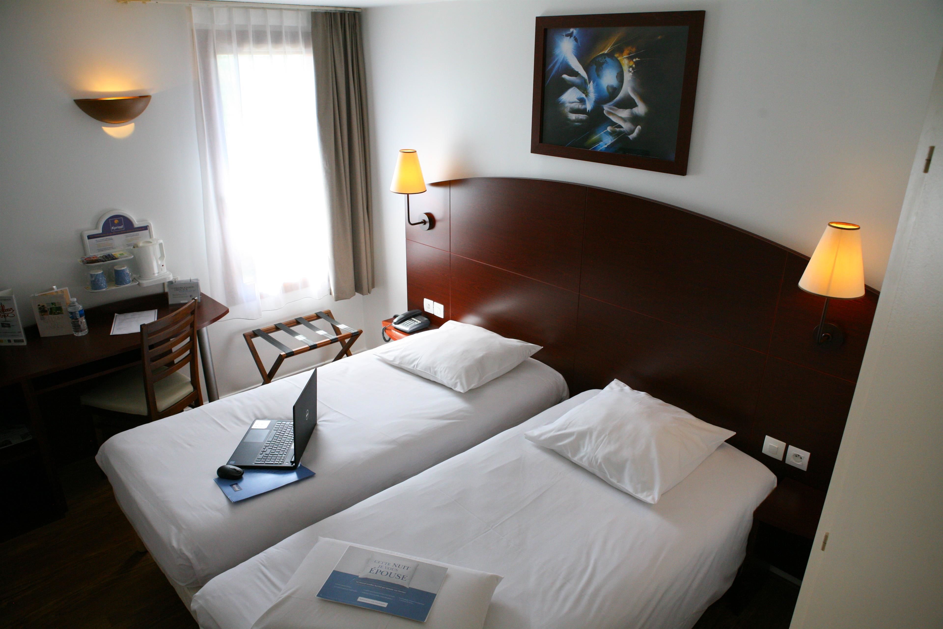 Une chambre d’hôtel avec deux lits, un bureau avec un ordinateur portable, une chaise et un tableau au mur.