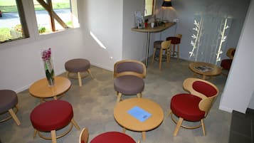 Een kamer met ronde tafels en stoelen, een klein tafeltje met een bloevas, en een raam met uitzicht op het buitengebied.