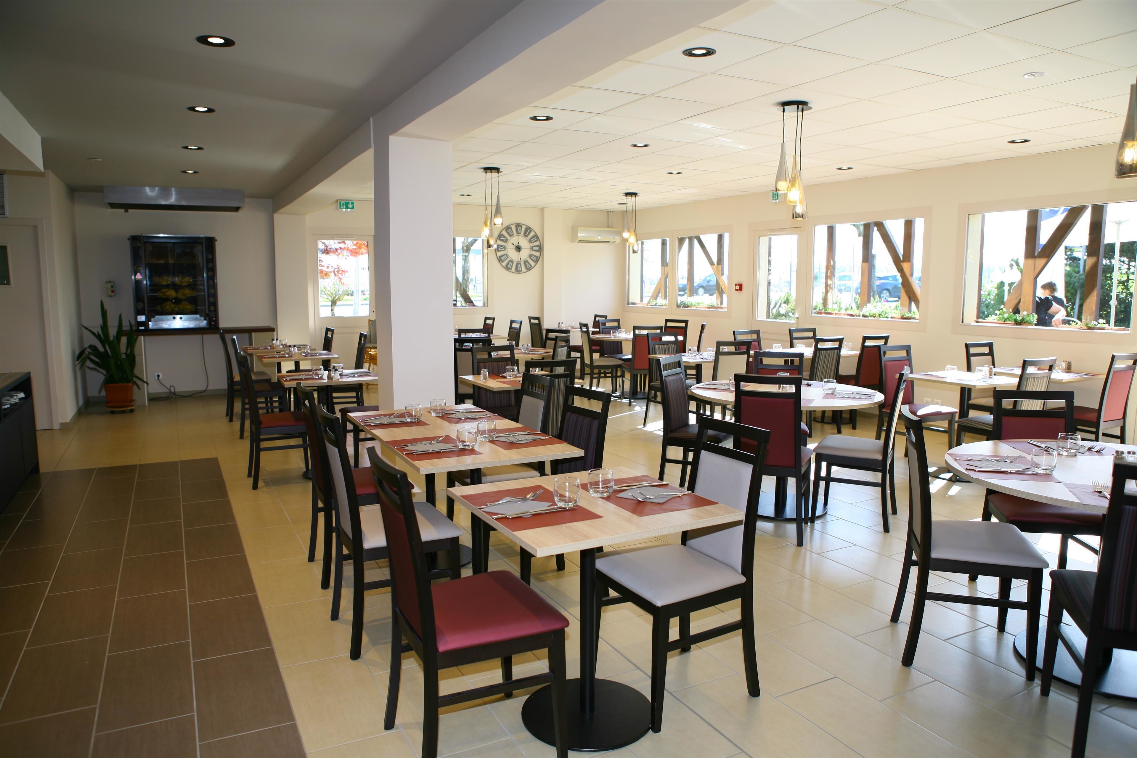 A spacious restaurant with multiple tables and chairs, large windows, and a clock on the wall.