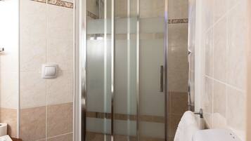 Une salle de bain avec une douche à parois de verre, des toilettes, un lavabo avec un distributeur de savon et un porte-serviettes.