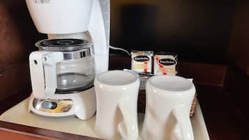 A coffee maker with two mugs and two packets of coffee additions on a tray.