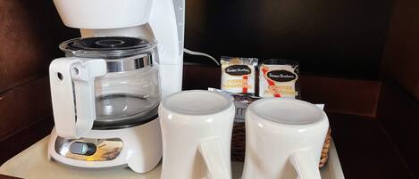 A coffee maker with two mugs and two packets of coffee additions on a tray.