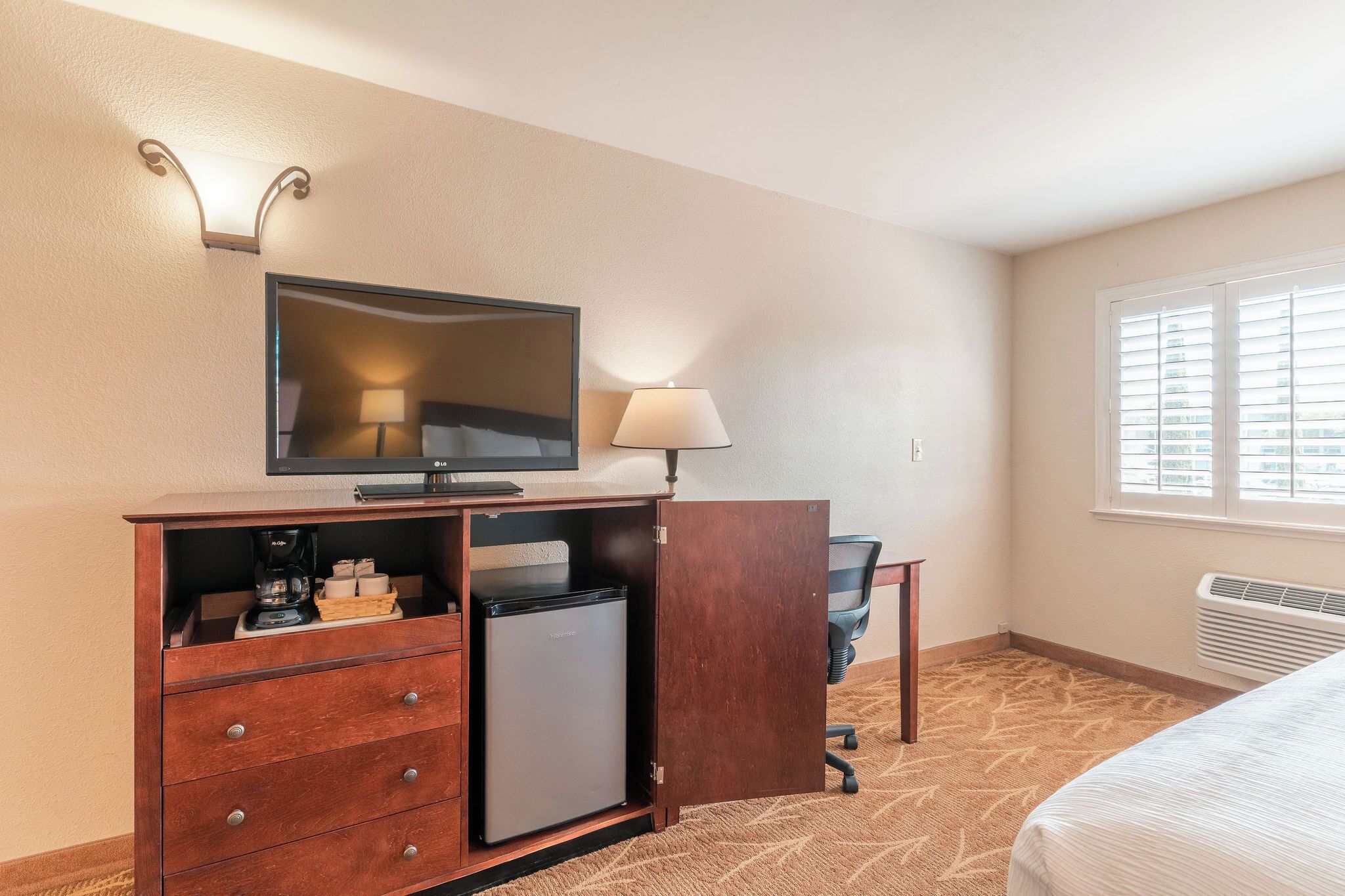 Une chambre d’hôtel équipée d’un lit, d’une télévision, d’un bureau avec une lampe, d’un mini-réfrigérateur et d’un radiateur.