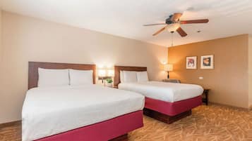 A hotel room with two beds, a ceiling fan, wall-mounted lamps, and a patterned carpet.