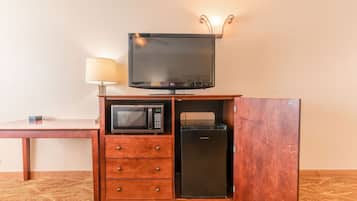 A compact kitchenette with a microwave, refrigerator, and a television on a wooden cabinet.