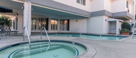 A swimming pool area with a covered deck, lounge chairs, and a staircase leading to an upper level.