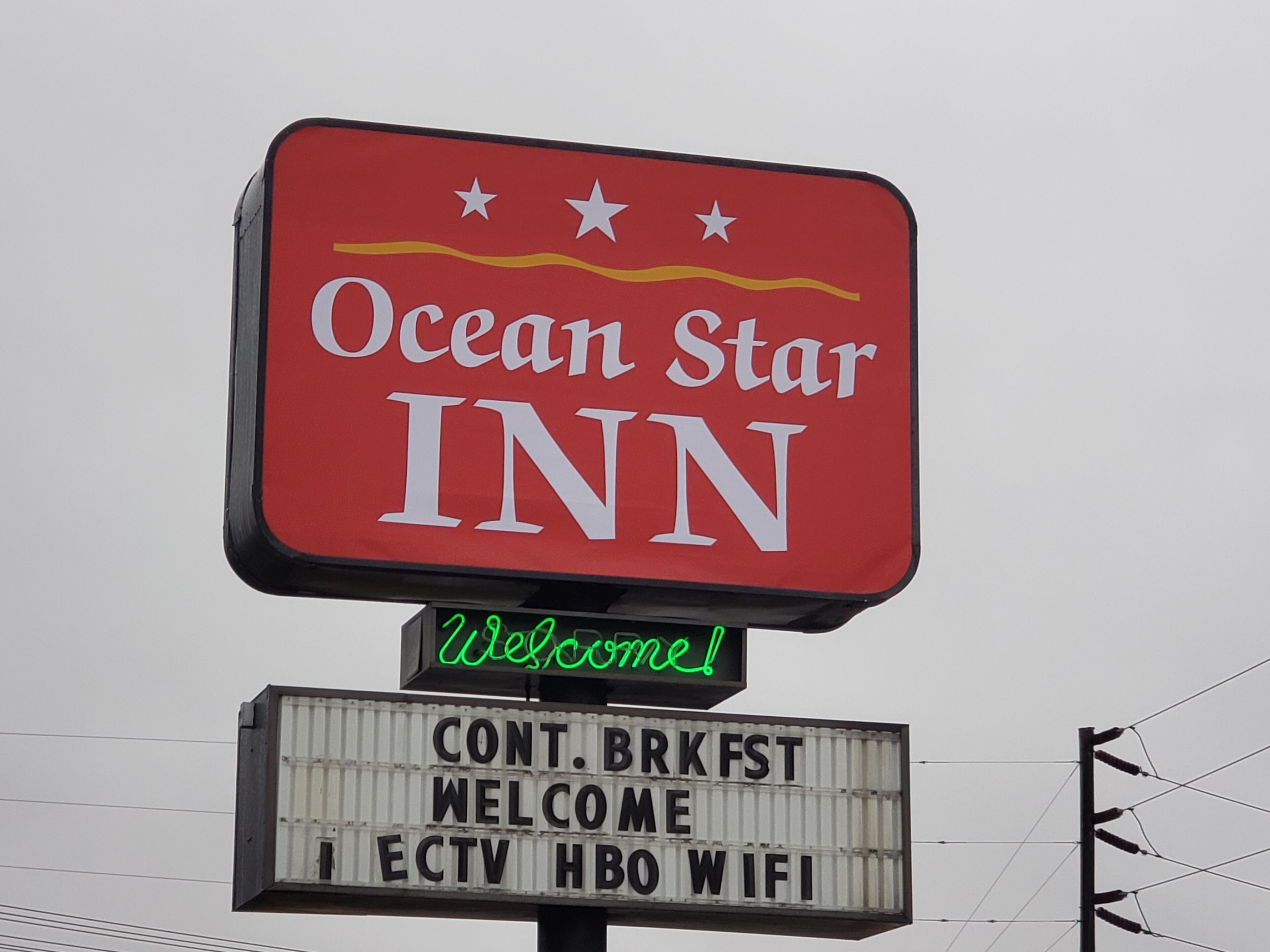 Señal del Ocean Star Inn con un mensaje de '¡Bienvenido!' y servicios enumerados abajo.
