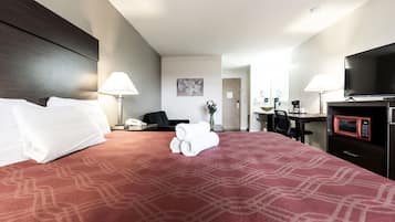Habitación de hotel con una cama grande, un escritorio con silla, televisor y microondas.
