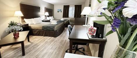 Habitación de hotel con cama, mesitas de noche, escritorio y una silla. Hay un jarrón con flores sobre el escritorio.