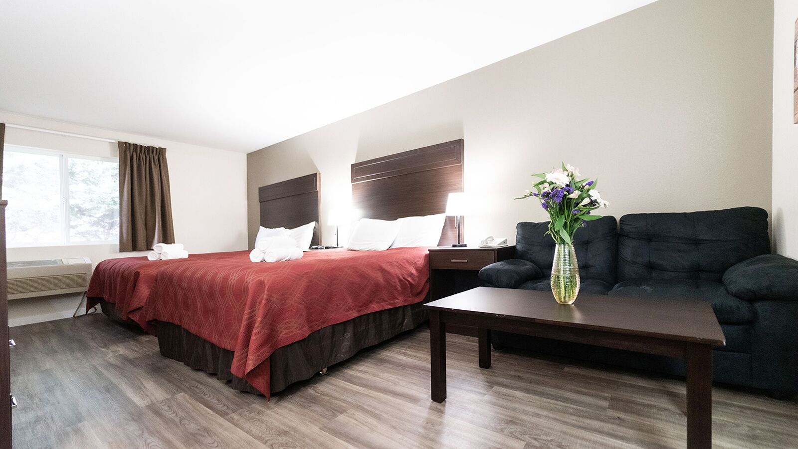 Een hotelkamer met een bed, een slaapbank, een salontafel en een vaas met bloemen.