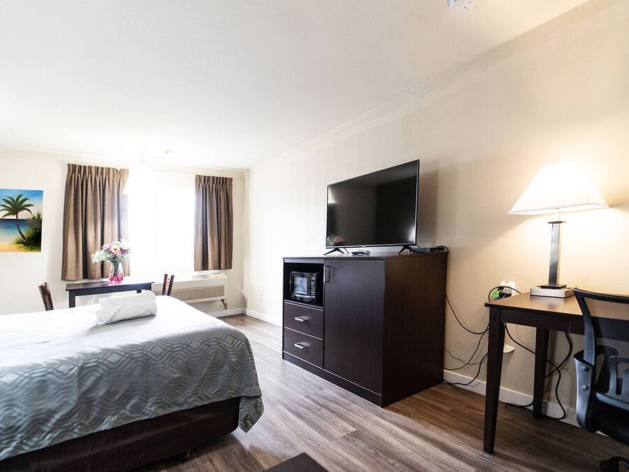 Et hotelværelse med en seng, et skrivebord med lampe, et fjernsyn og et maleri på væggen.