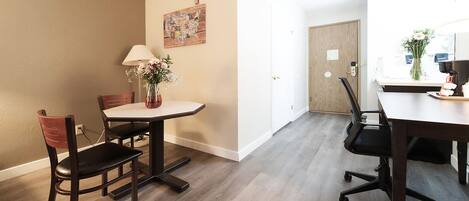 Una cocina moderna con encimera blanca, una mesa de comedor de madera y sillas. Hay un jarrón con flores sobre la encimera.