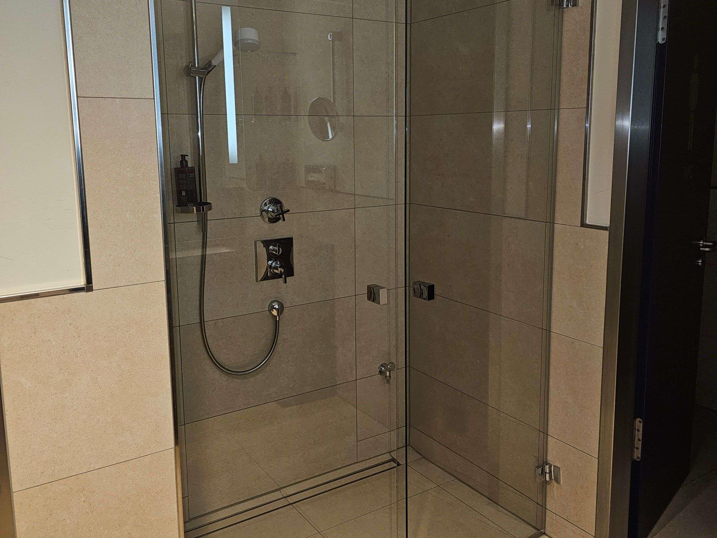 A glass-enclosed shower with a handheld showerhead, a wall-mounted control panel, and a tiled floor.