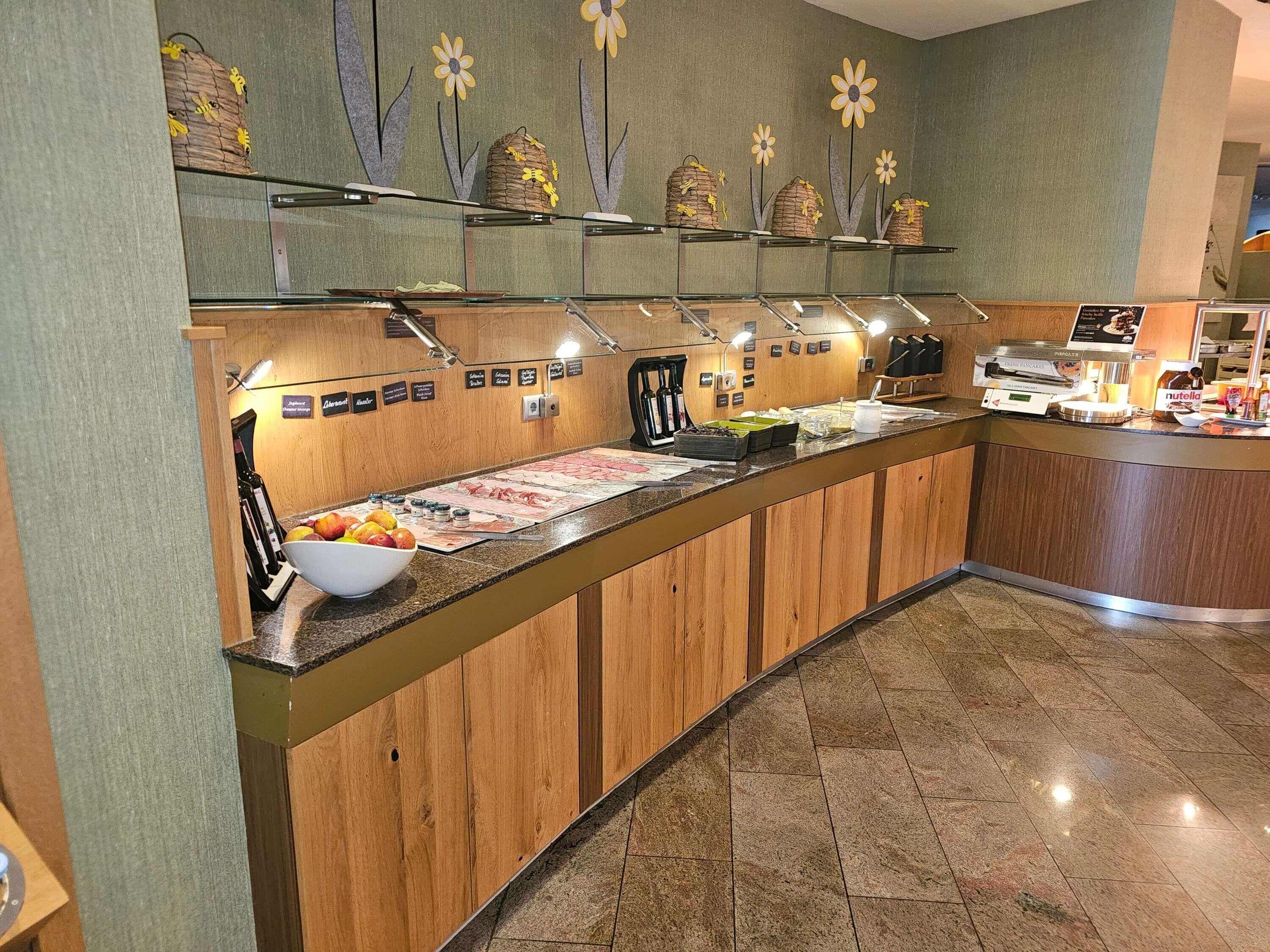Zona de bufé con mostrador de madera, diferentes opciones de comida y una pared decorada con motivos florales.