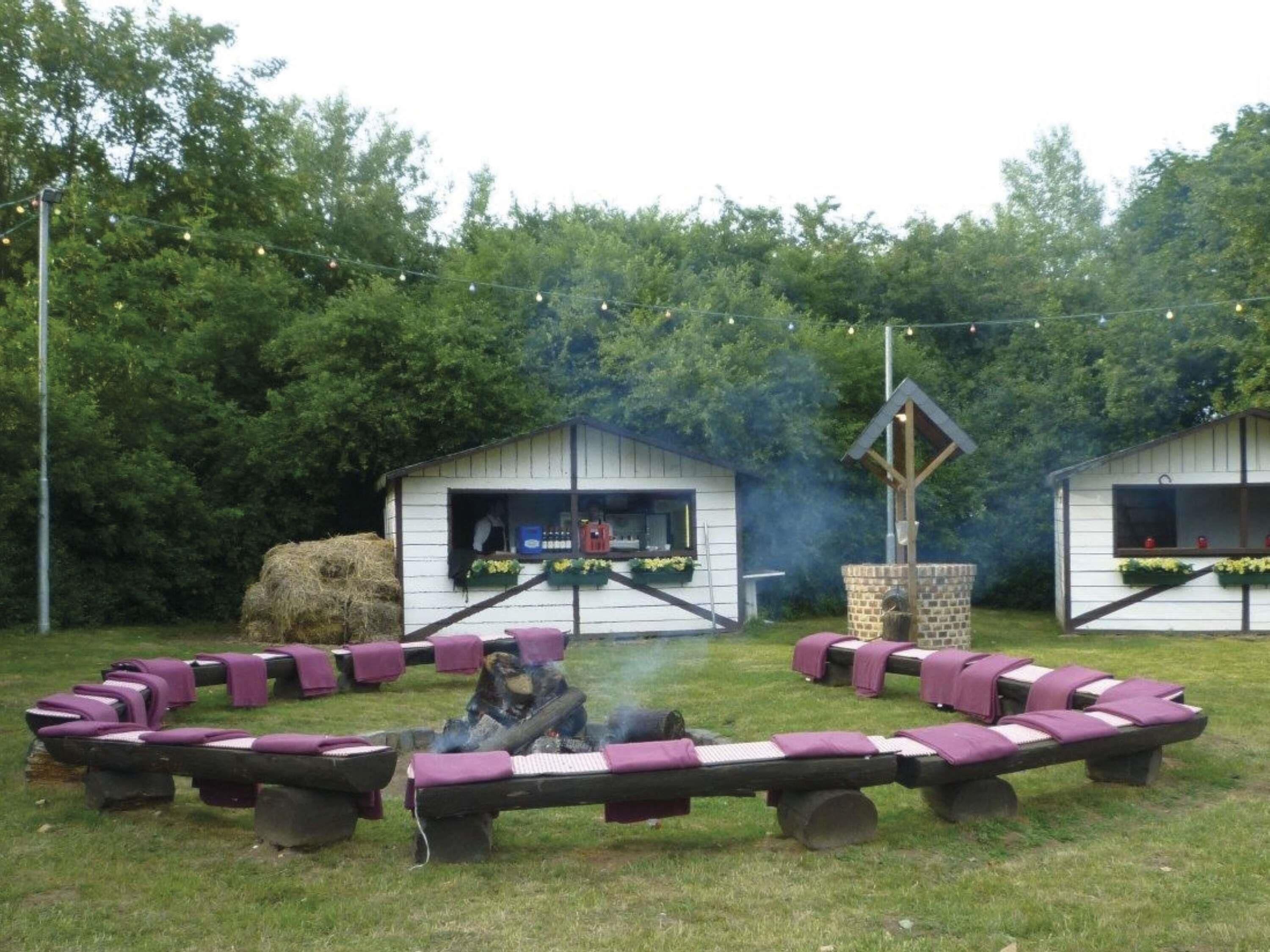 A circular seating area with benches and a central fire feature, surrounded by two white buildings with windows and flower boxes.