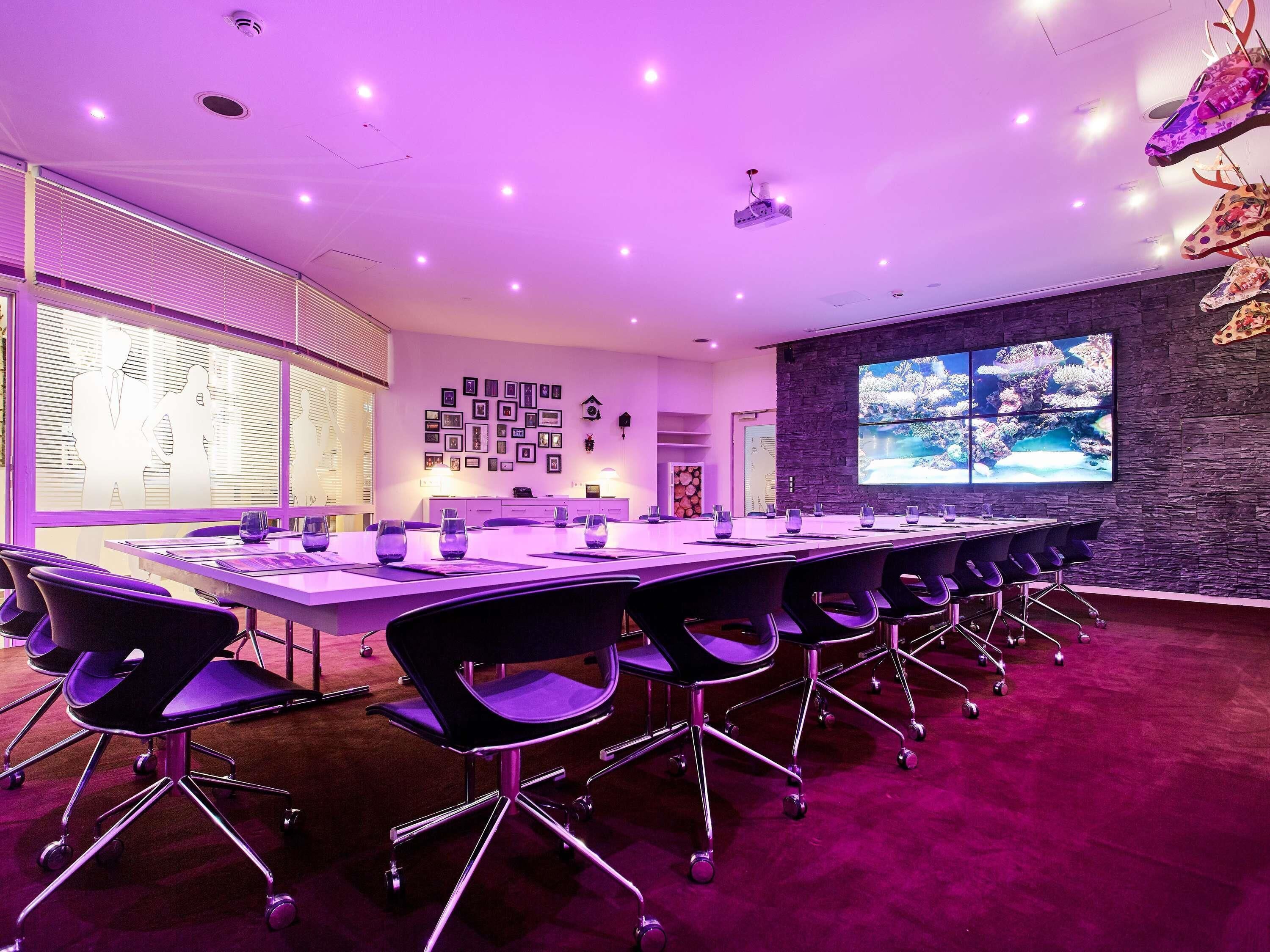 A conference room with a long table, chairs, a projector, and a large screen.