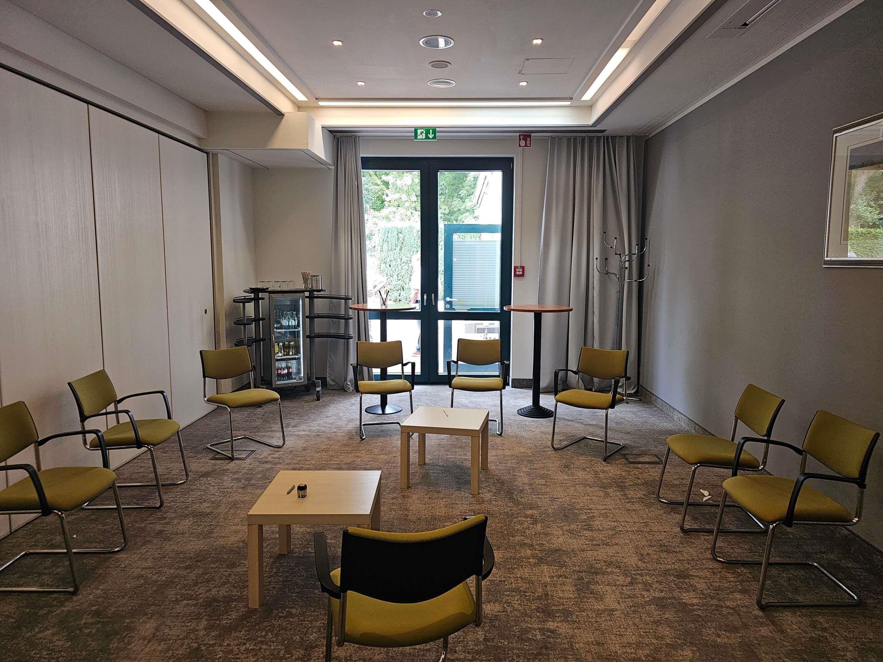 Una sala conferenze con un tavolo, sedie, un piccolo carrello bar e vista attraverso una porta.