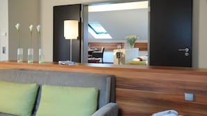 A modern hotel room with a grey sofa, a wooden headboard, and a skylight. - Mercure Tagungs- & Landhotel Krefeld (Krefeld)