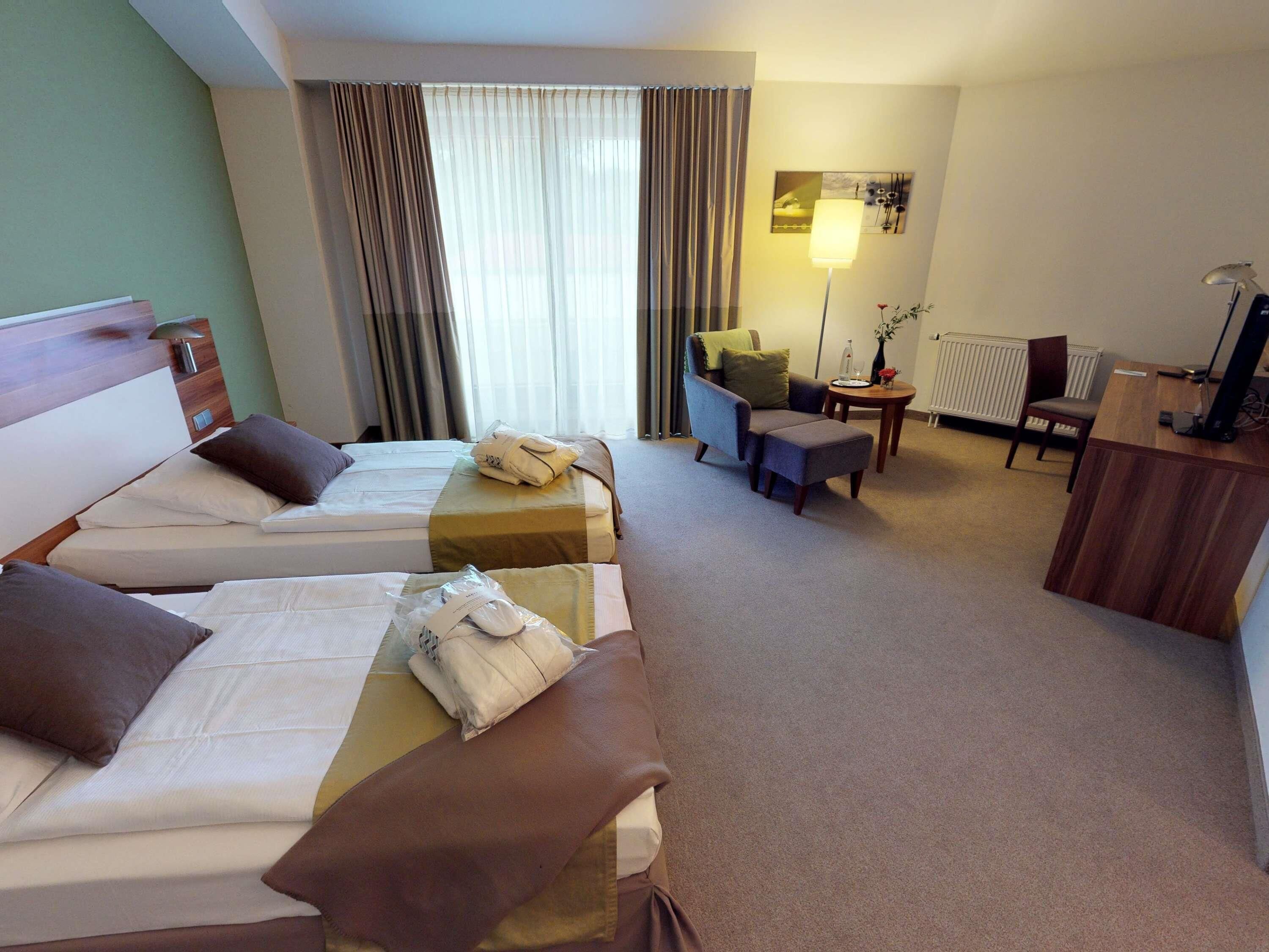 A hotel room with two beds, a desk, a chair, a lamp, and a radiator.