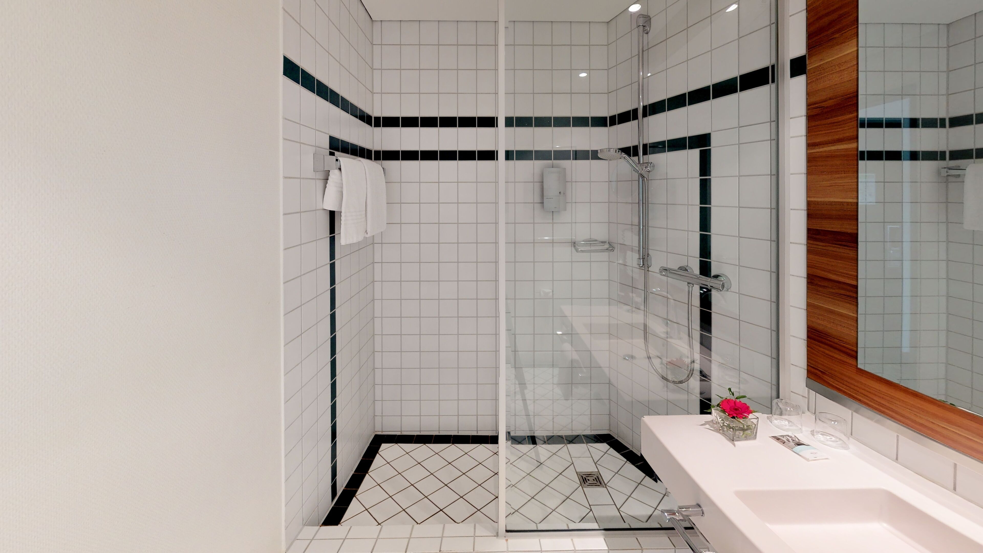 A modern bathroom with a glass-enclosed shower, white tiles, and a wooden vanity with a mirror.