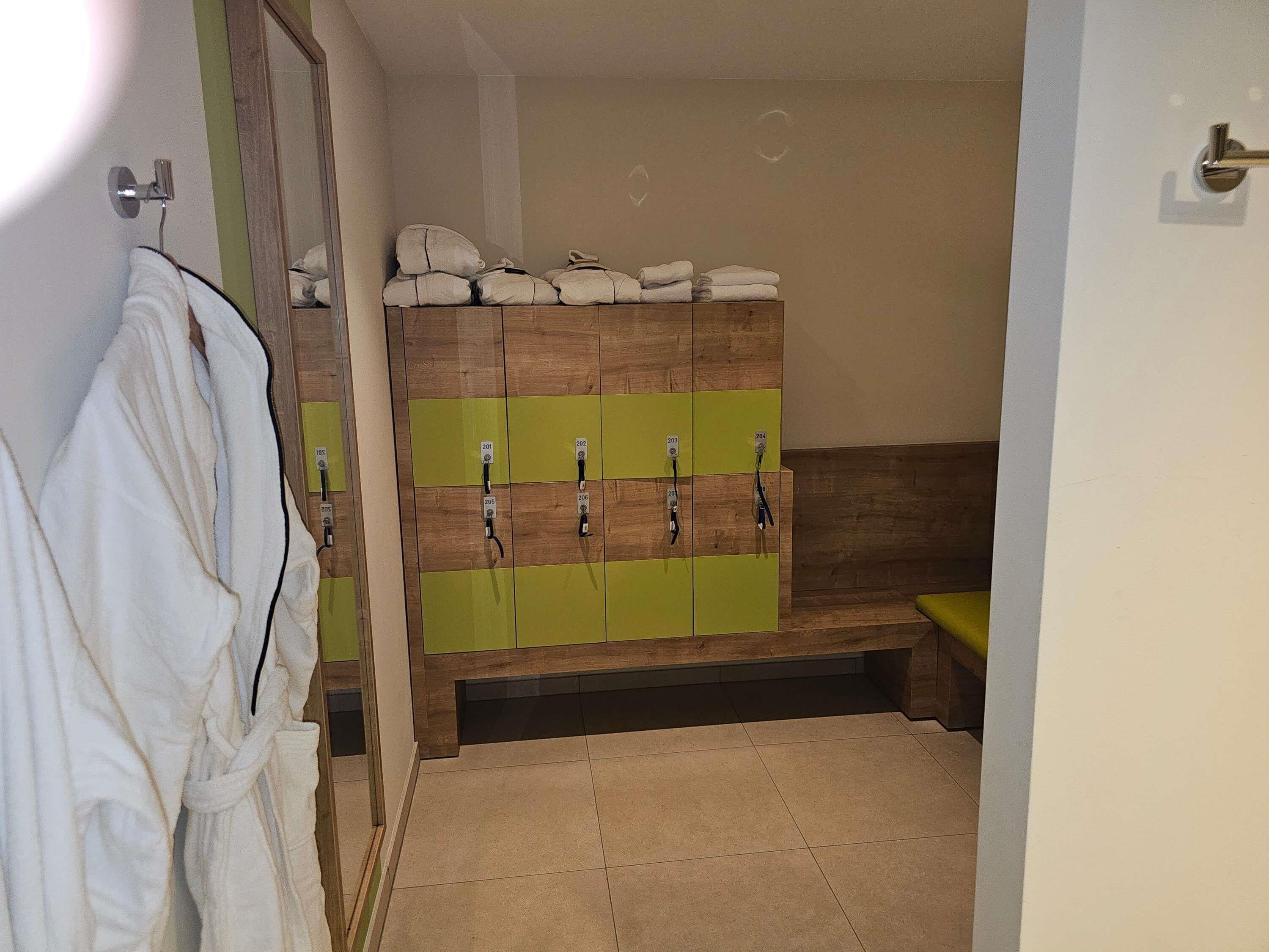 Un baño con un banco de madera, un perchero con toallas y un espejo.